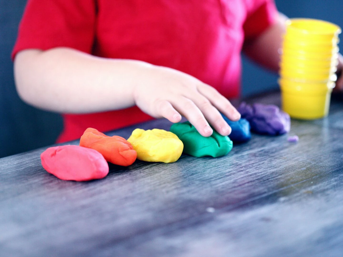 a young child with rainbowcolored modeling clay and stacking cups on a table indoors