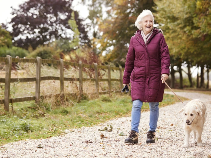 active senior woman on autumn walk with dog on path through countryside