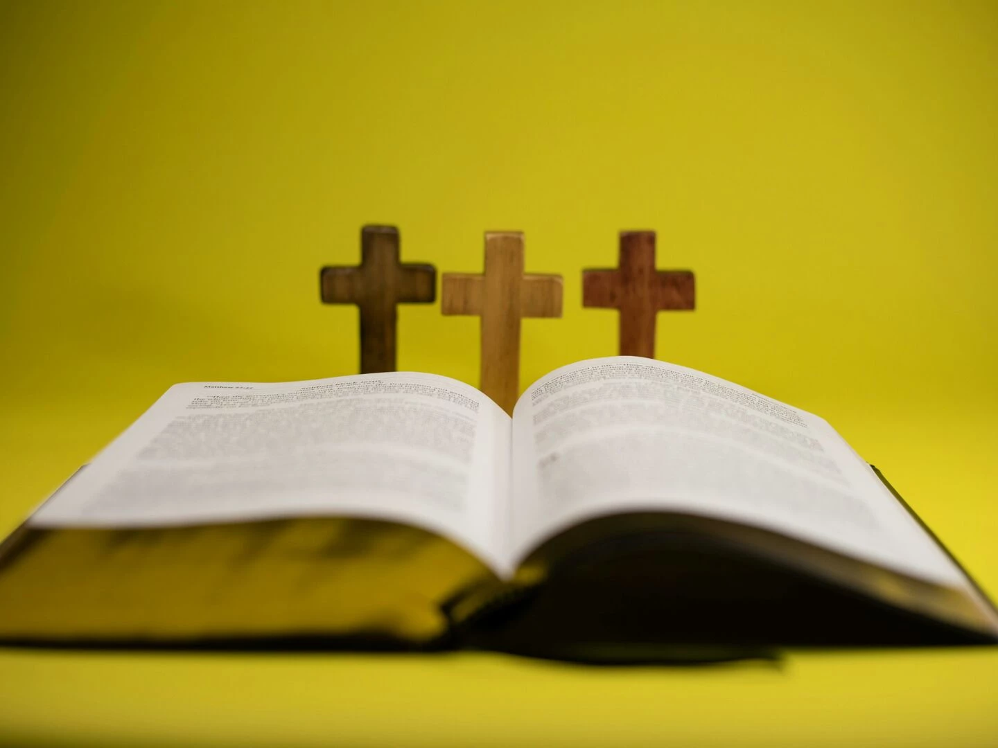 an open bible with three crosses displayed against a vibrant yellow backdrop
