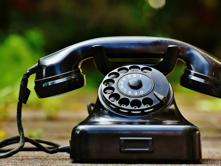 Close-up of a classic black rotary phone outdoors with a blurred green background.