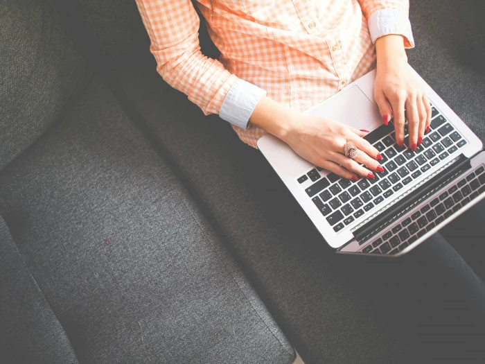 Person Sitting on Gray Sofa While Using Macbook