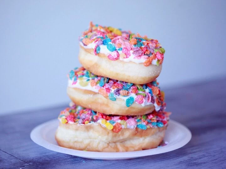 A stack of doughnuts covered in colorful fruity pebbles on a plate.