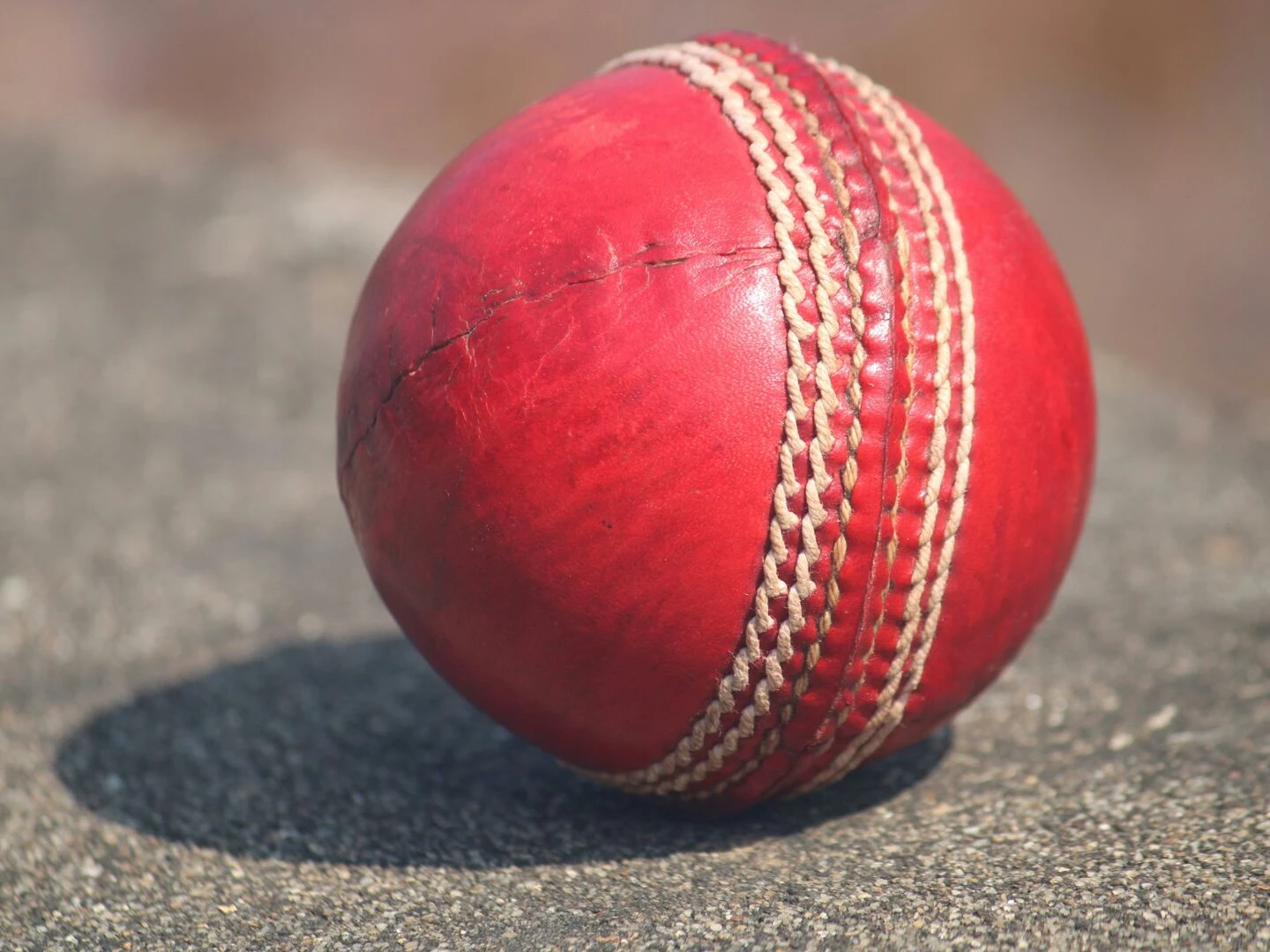 detailed view of a textured red cricket ball outdoors in sunlight