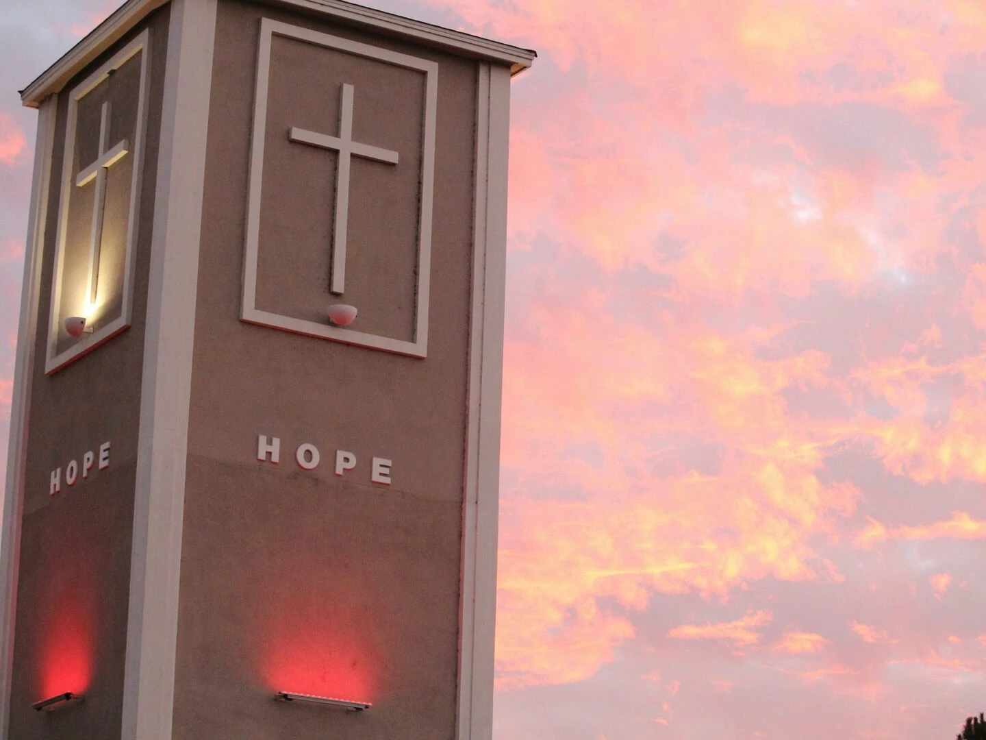 illuminated church tower with crosses against a vibrant sunset sky