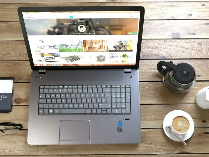 silver laptop next to coffe cup smartphone and gla